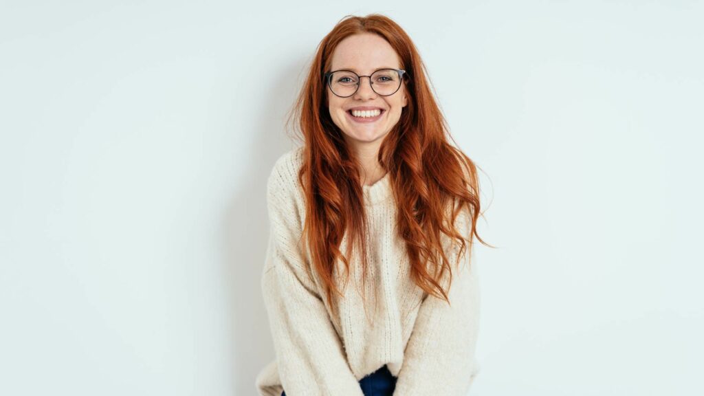 Giovane ragazza sorridente con maglione bianco su sfondo bianco